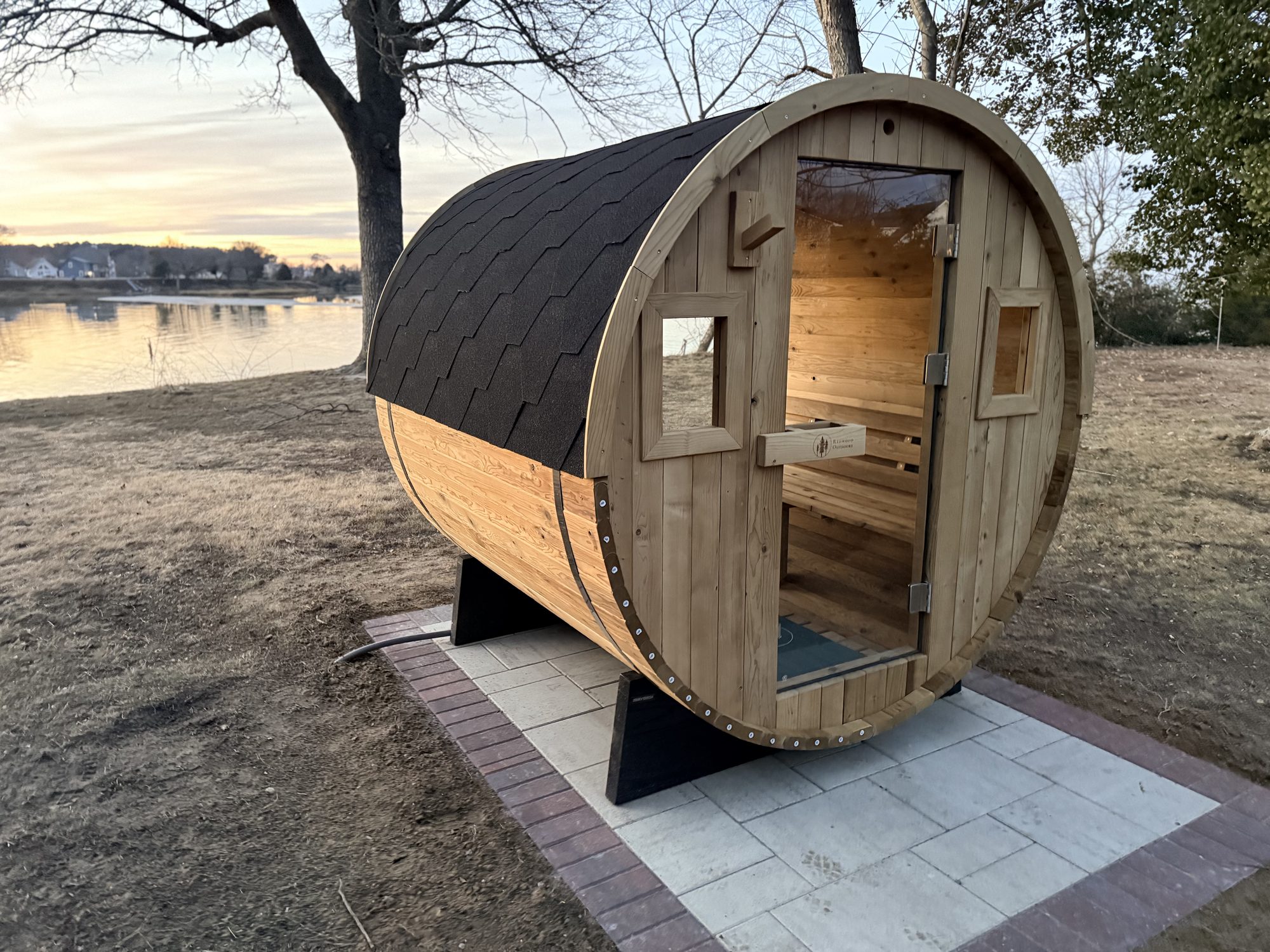 The cedar barrel sauna at Captain's Cottage on Hull Creek, lit by late-afternoon sun with the creek and treeline behind.