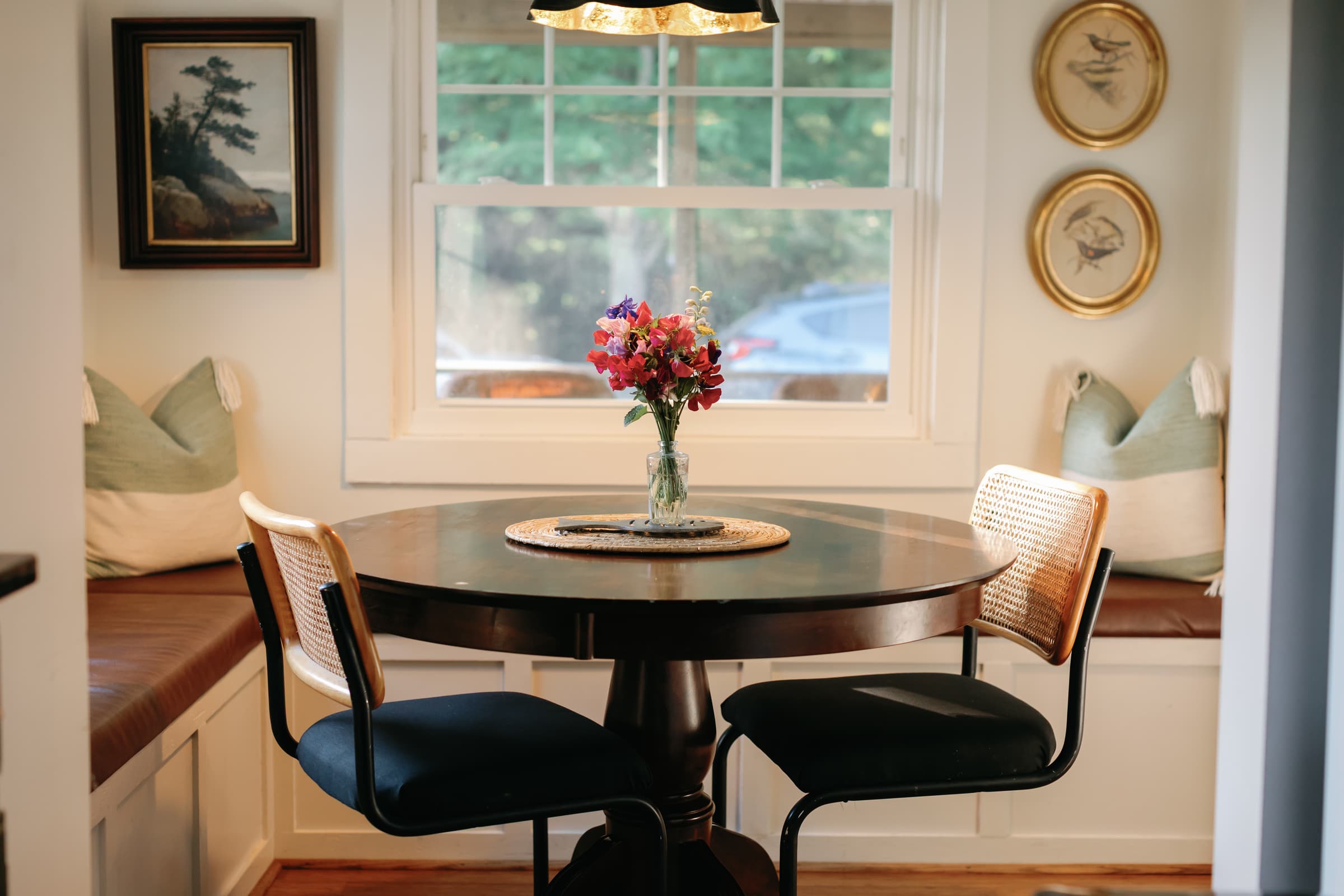 The breakfast nook off the kitchen at Captain's Cottage — a round table and banquette bench beneath a pendant light.