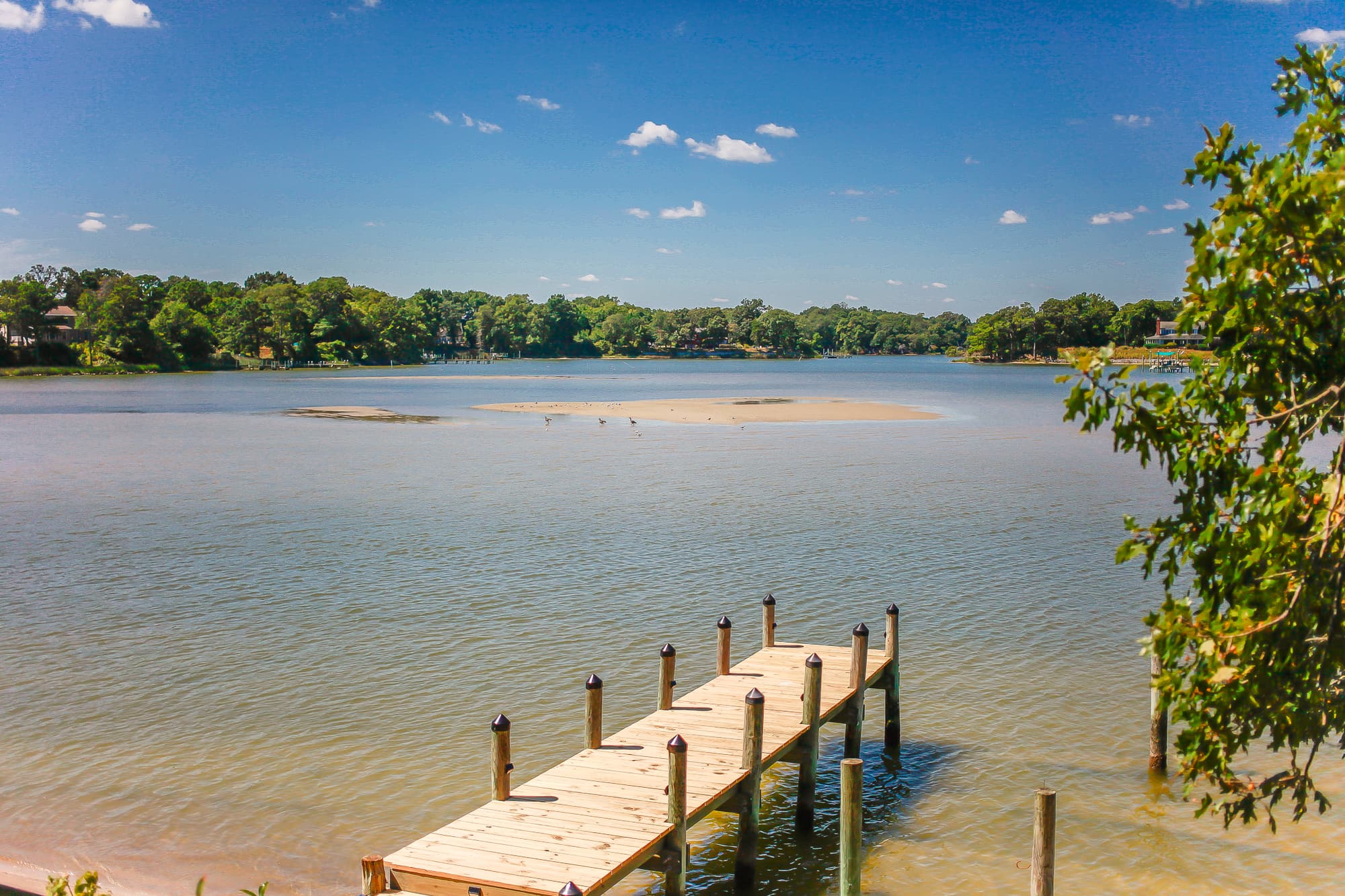 Private dock at Captain's Cottage extending into Hull Creek, with a sandbar visible mid-creek and a far tree line on the opposite shore.