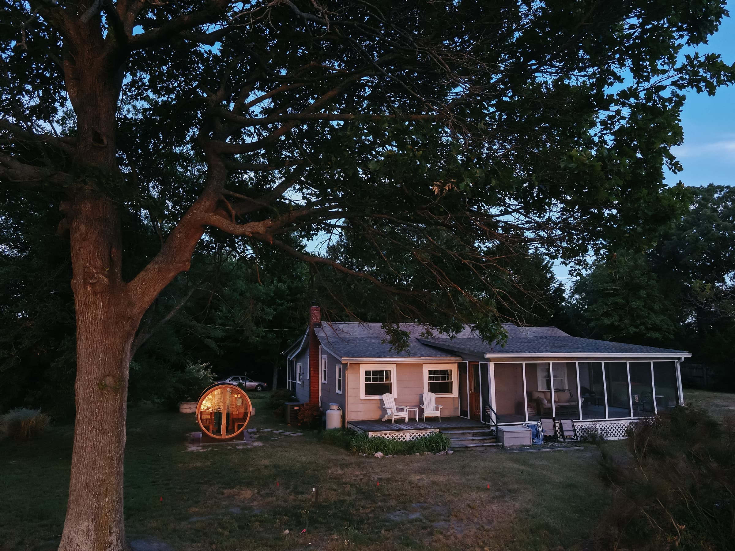 Aerial view of Captain's Cottage at dusk, the lit cedar sauna glowing beside the cottage with Hull Creek beyond.