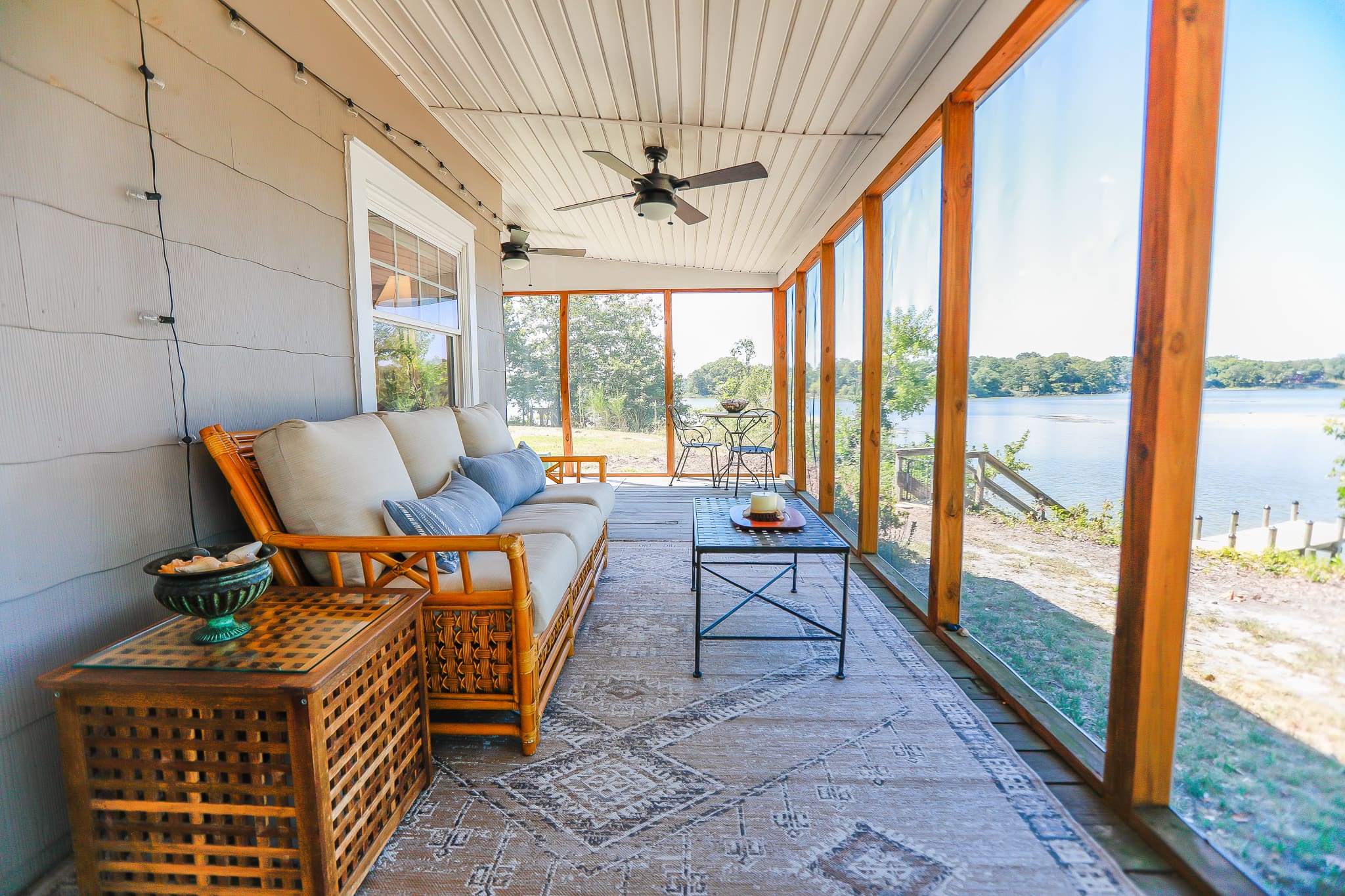 The rattan-furnished screened porch at Captain's Cottage looking out over Hull Creek — cedar-framed screens, ceiling fans, and water beyond in Heathsville, Virginia.