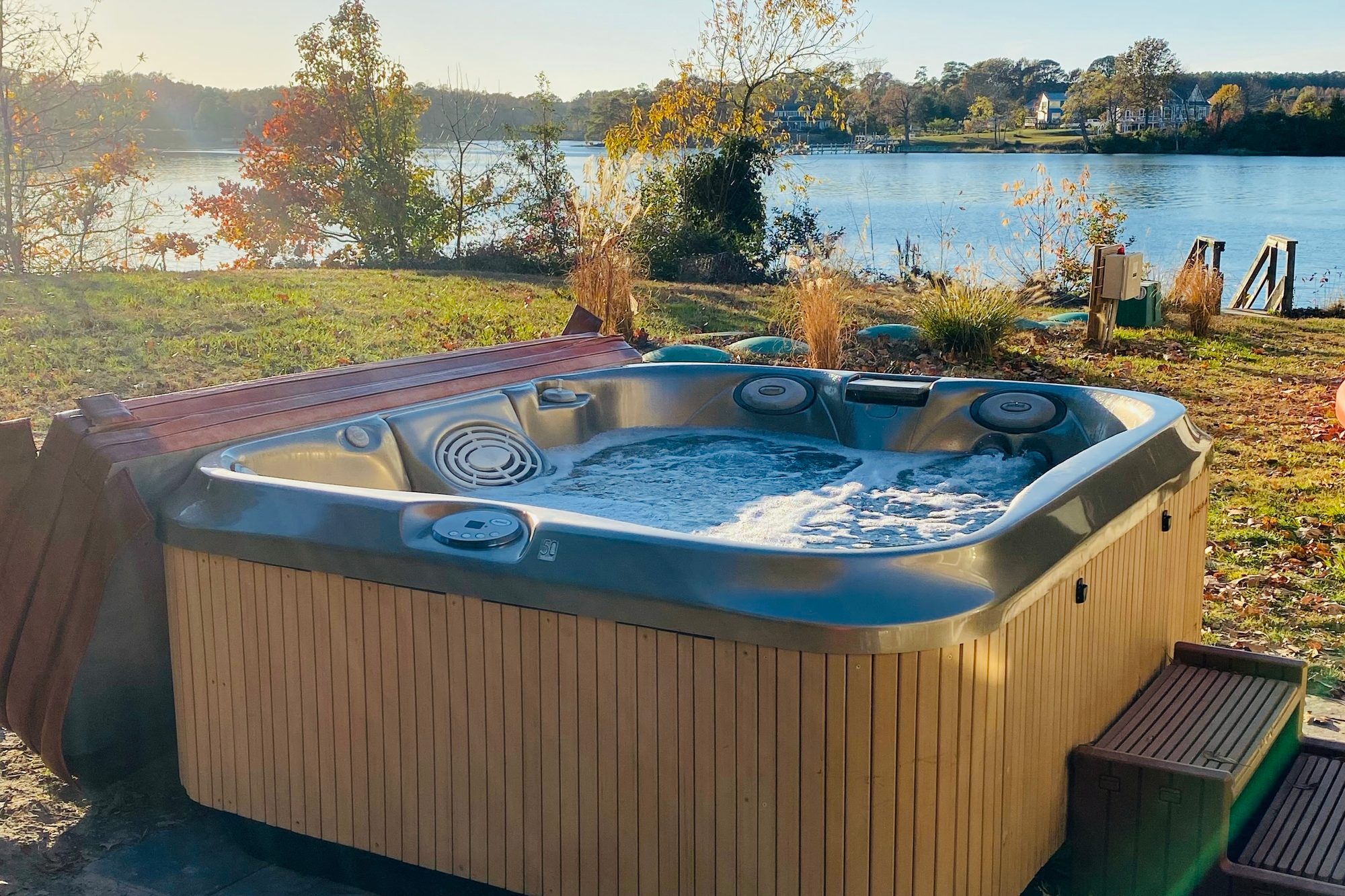 Hot tub on the back deck at Captain's Cottage, bubbling water in the foreground, Hull Creek and the dock just beyond in autumn light.