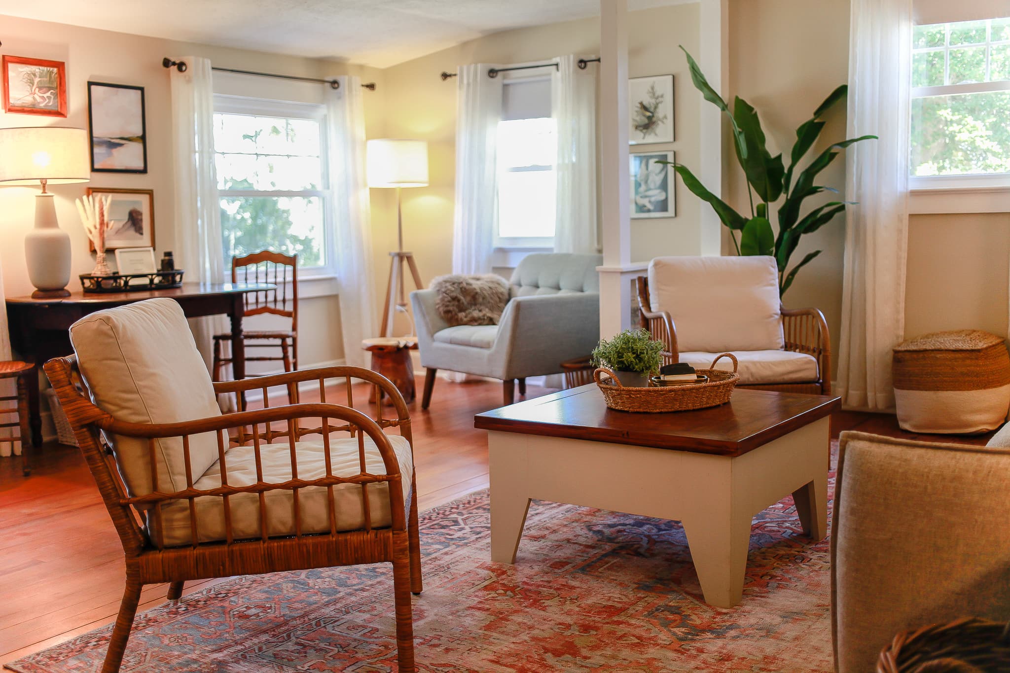 Living room at Captain's Cottage — rattan chairs, a vintage red rug, and the dining nook beyond.