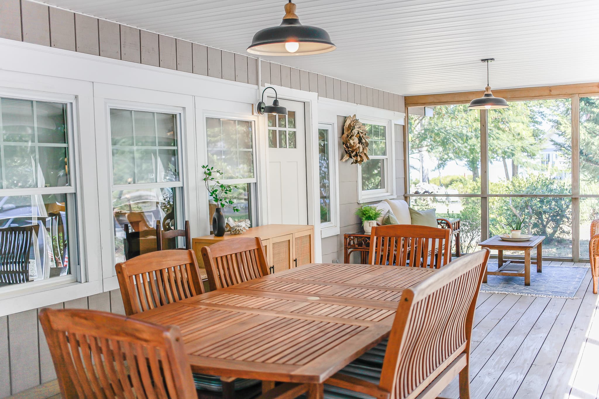 Wooden dining table on the screened porch at Captain's Cottage, with pendant lights and white siding.