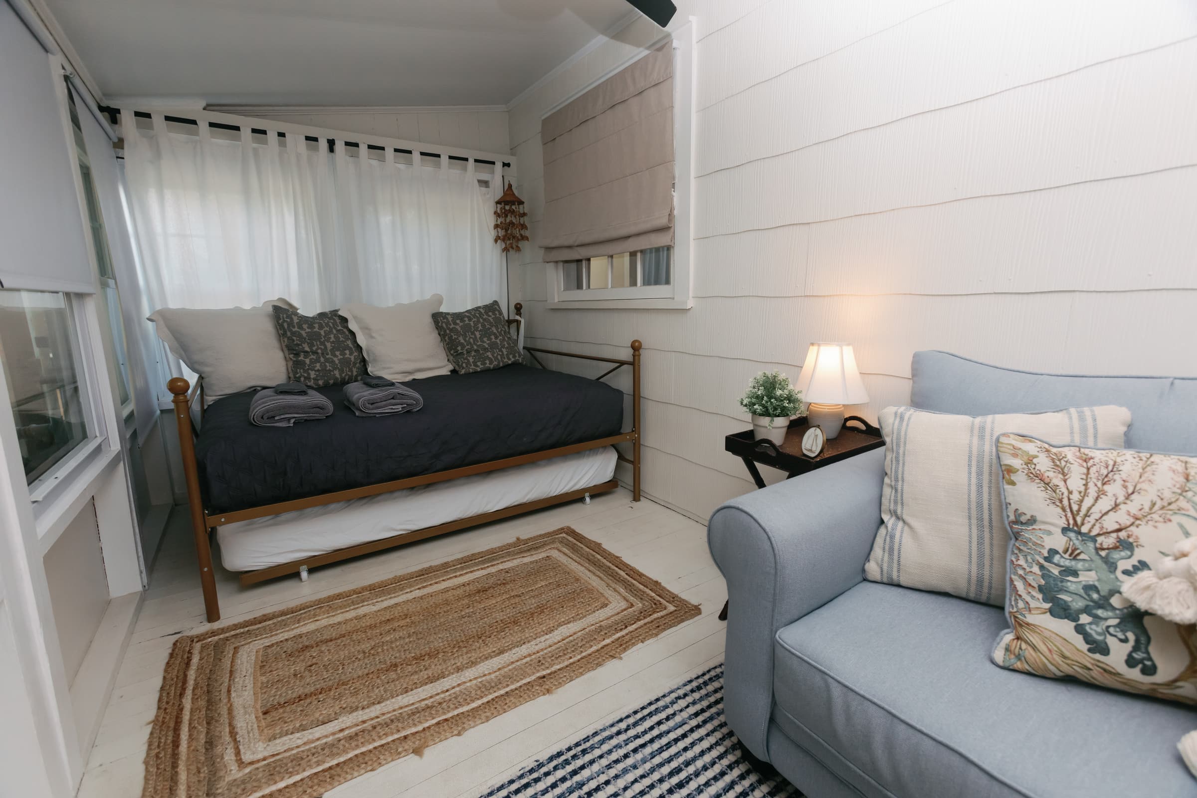 The sleeping porch at Captain's Cottage — a sunroom third bedroom with a brass daybed and trundle, windows on three sides.